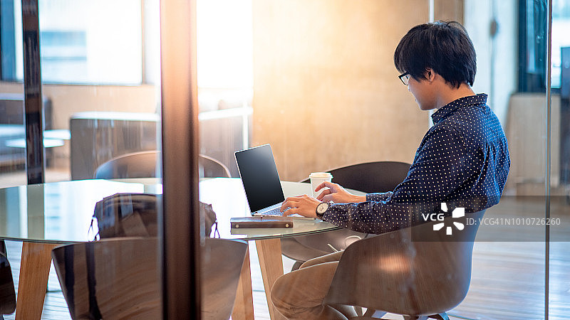 年轻的亚洲商人在办公室会议室里使用笔记本电脑。在迷你会议室工作的男性企业家。城市生活方式的概念图片素材
