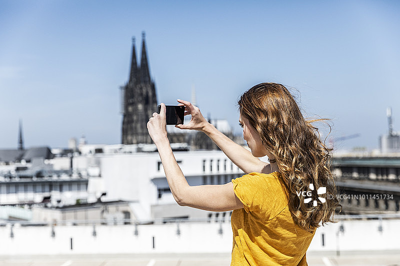 德国，科隆，一名女子在屋顶露台上用智能手机拍照图片素材