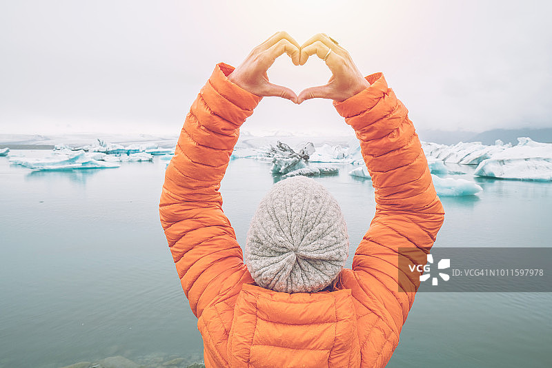 在冰岛的冰川泻湖上，一名年轻女子正在制作心形手指架图片素材