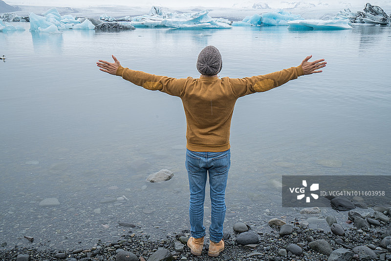 青年男子双臂伸向冰岛冰川泻湖，游客男子旅游自由畅快享受北欧自然环境理念图片素材