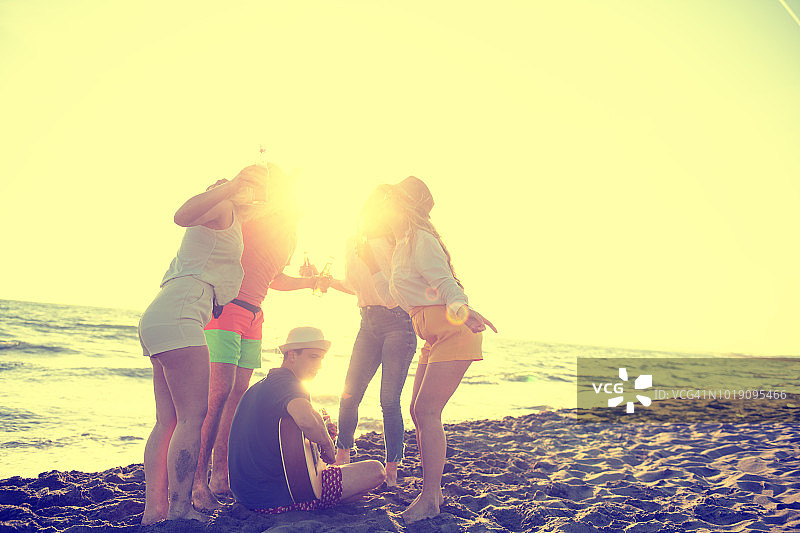 一群快乐的年轻人在美丽的夏日日落的海滩上跳舞图片素材