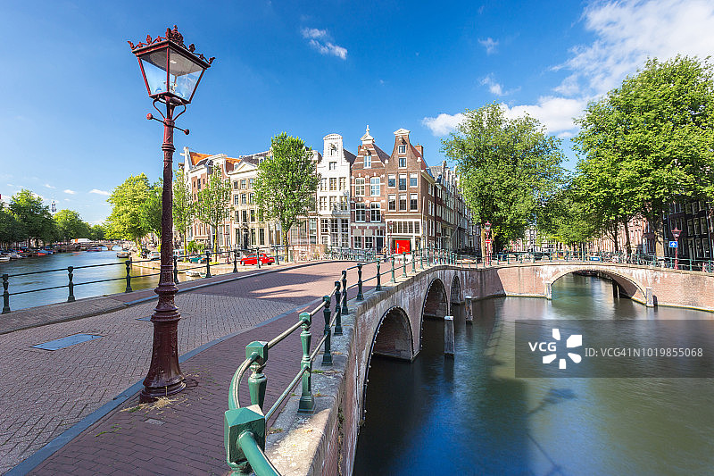 著名的桥和公寓沿着运河或河流，在阿姆斯特丹市，荷兰，欧洲的游轮和船运输图片素材