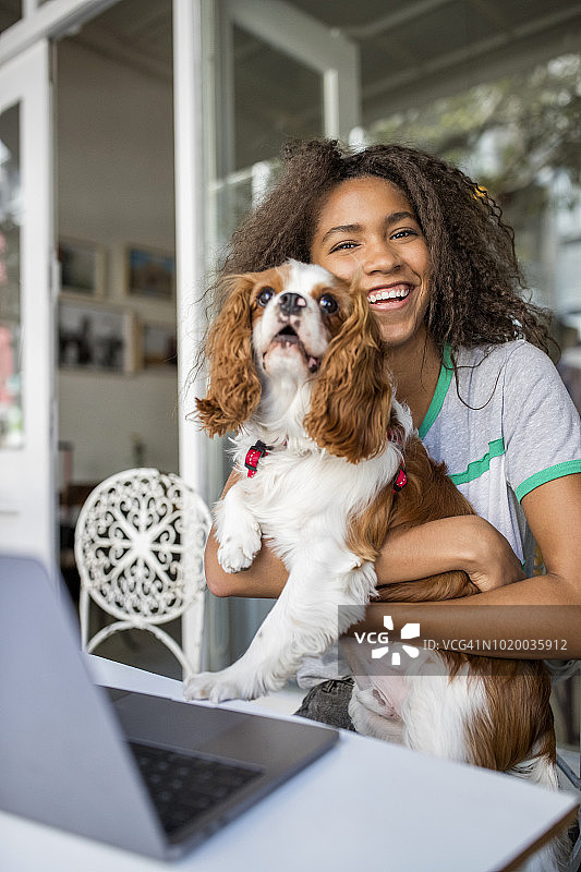 一个快乐的年轻女人带着狗和笔记本电脑在一个户外咖啡馆图片素材