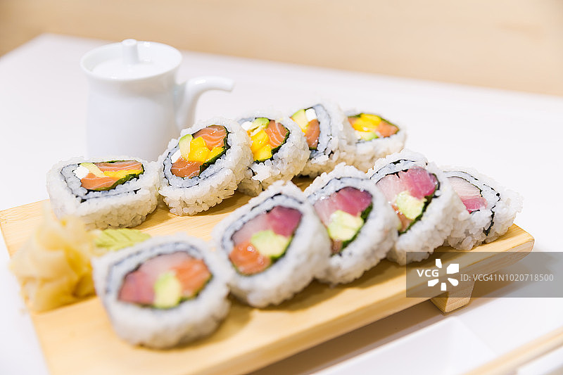 一个竹切板和两个寿司卷，金枪鱼，鲑鱼，黄尾加利福尼亚风格图片素材