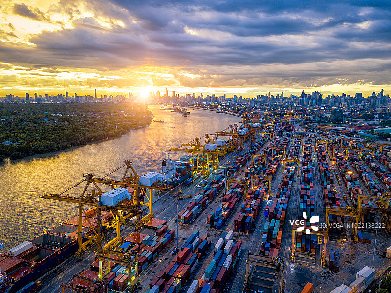 国际港口用起重机装载集装箱的进出口业务物流鸟瞰图与夕阳下的泰国曼谷城市景观图片素材