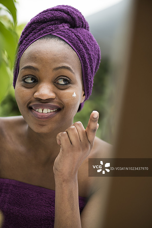 一名年轻的非洲女子在浴室里给脸涂保湿霜图片素材
