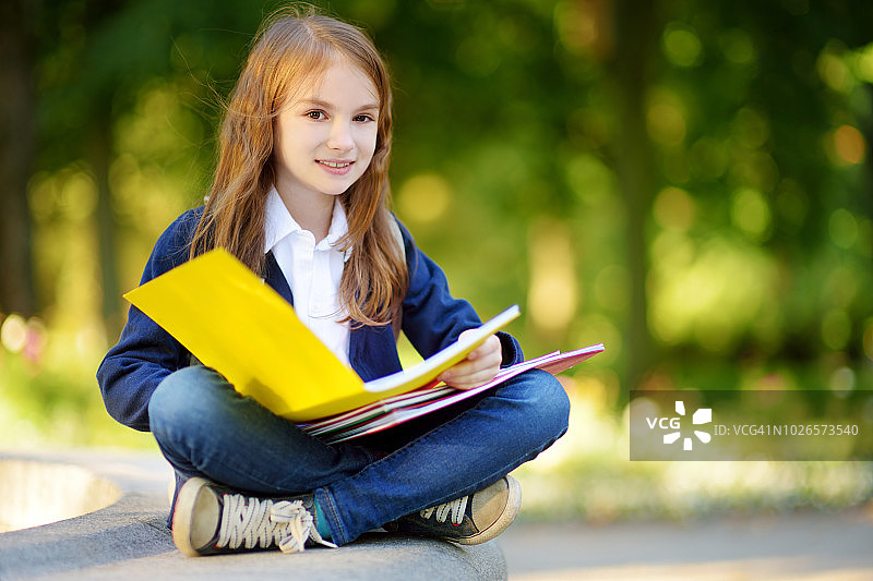 可爱的小女孩在晴朗的秋日在户外学习。年轻的学生在做她的家庭作业。对小孩子的教育。图片素材