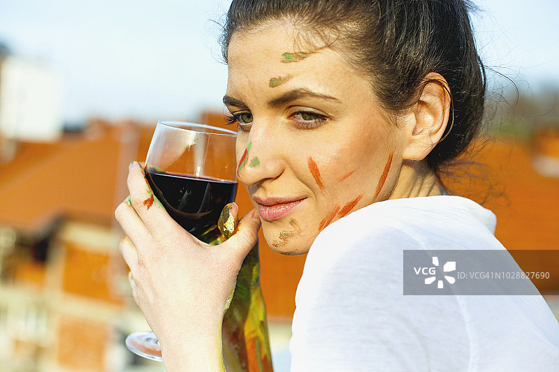 一个微笑的年轻女艺术家举着一杯红酒的肖像图片素材