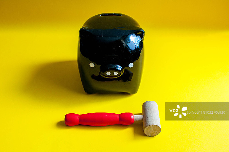 黑色的储蓄罐和木制的锤子映衬着黄色的背景图片素材
