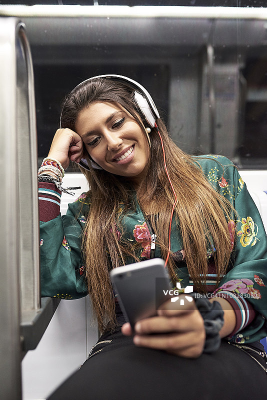 微笑的女人戴着耳机在地铁里看手机的肖像图片素材