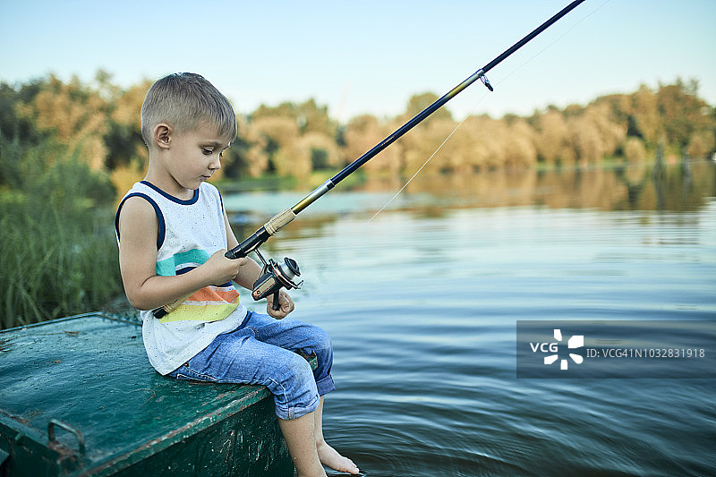 小男孩拿着钓竿坐在船上的背影图片素材