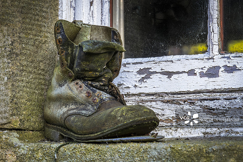 一只旧靴子放在一扇饱经风霜的窗户外面的混凝土窗台上图片素材
