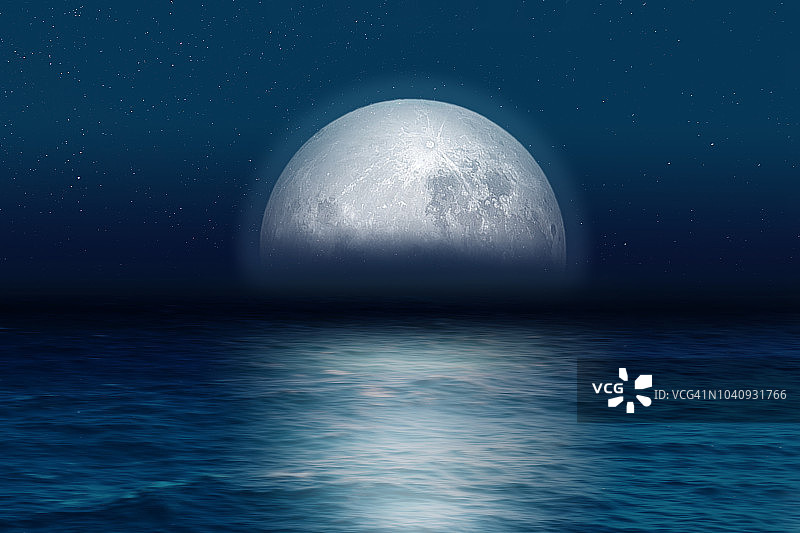 蓝月亮在夜晚从海上升起。图片素材