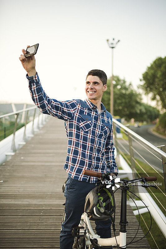 微笑的年轻人与折叠自行车在桥上自拍图片素材