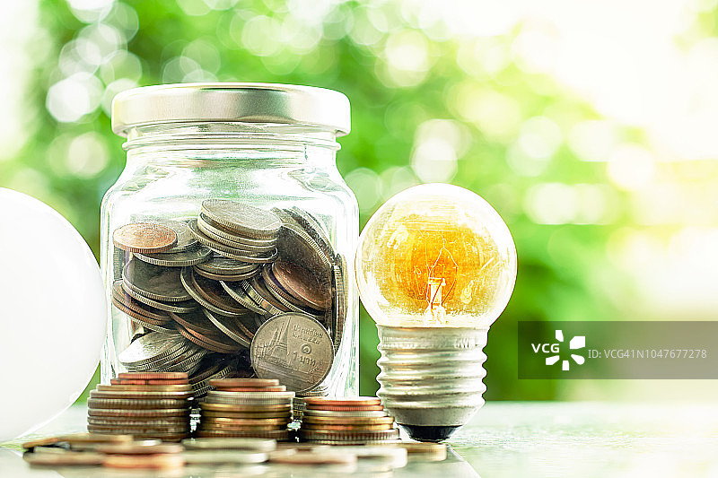 发光的灯泡和led灯与硬币在玻璃罐内以模糊的自然绿色背景为金融，节能环保的理念图片素材