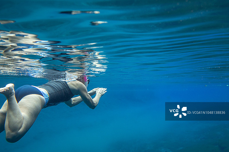 50多岁的健康和活跃的女性在节假日在蓝洞的水里游泳。穿比基尼底，穿无袖泳衣，做蛙泳。用右边的拷贝空间填充框架的左边。美丽的碧水图片素材