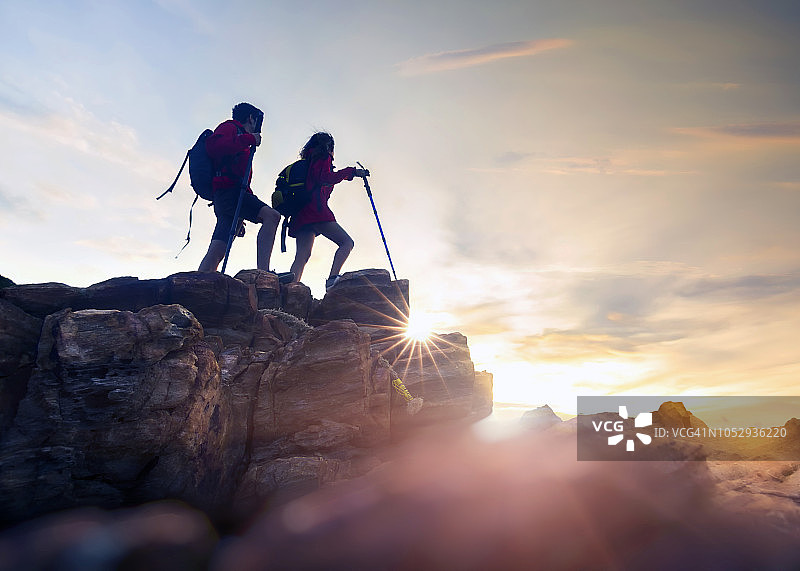 一对年轻的徒步旅行者在日落时分爬上了岩石山的顶峰图片素材
