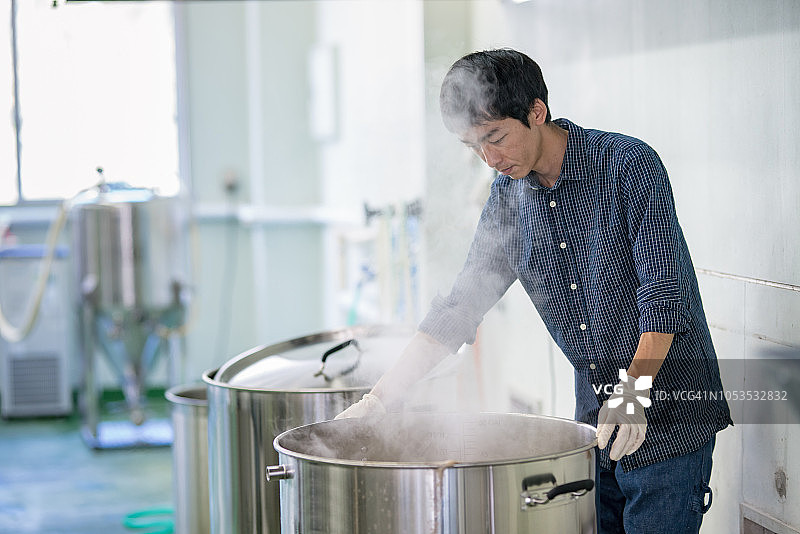 中年男子在一家精酿啤酒酿酒厂看着一个冒着热气的大桶图片素材