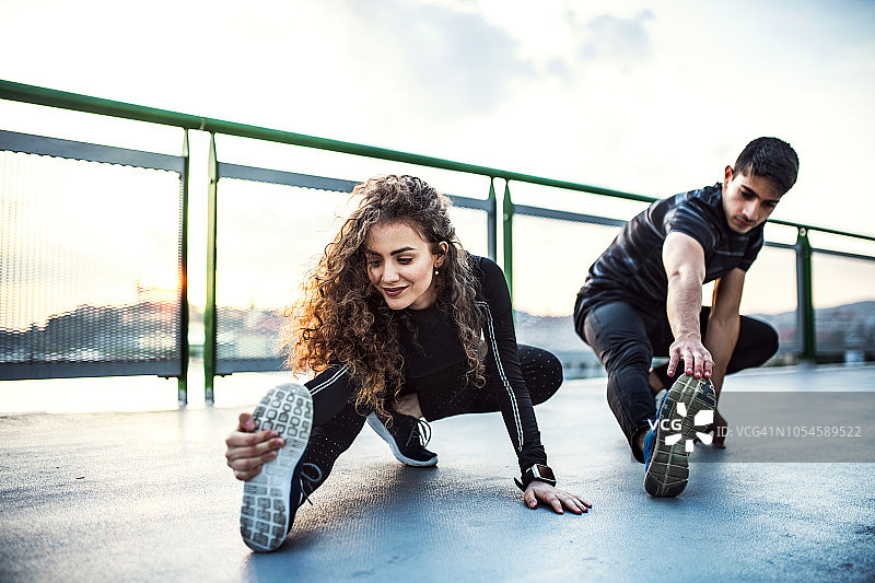一对运动的年轻夫妇在城市户外的一座桥上伸展四肢。图片素材