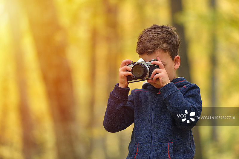创意儿童，儿童摄影师(一个小男孩)带着相机拍摄多彩的秋天森林图片素材