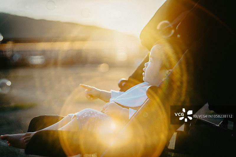 快乐的小女孩坐在婴儿车里，在美丽的夕阳下玩着漂浮的泡泡图片素材