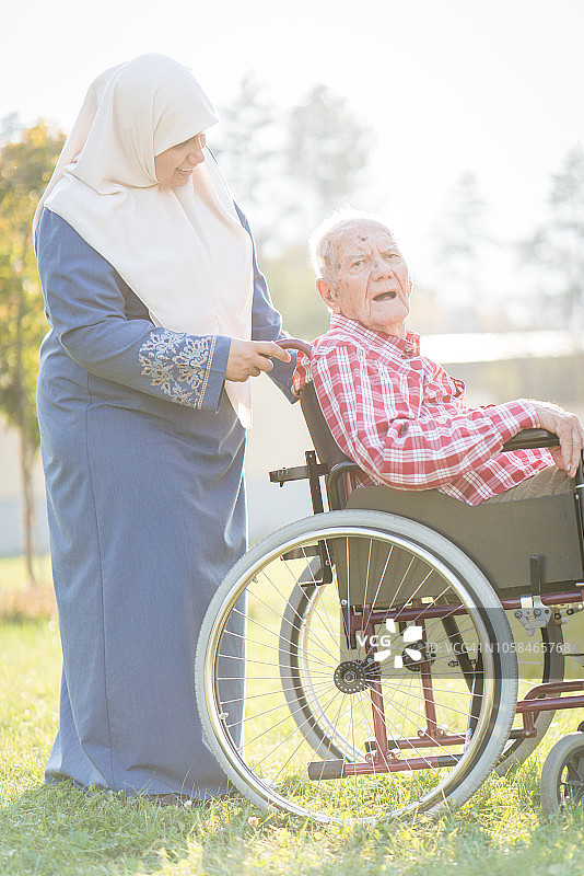一个坐轮椅的老人和一个在户外行走的女人图片素材