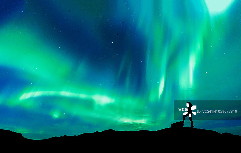 北极光以人的剪影站在山上。自由旅行者旅行概念图片素材