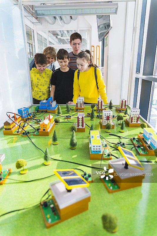 这个十几岁的男孩在科学技术大厅里用一个巨大的城市模型向一群孩子和成年人解释电力是如何工作的图片素材