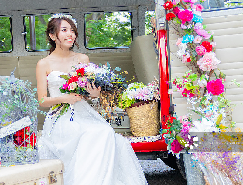 年轻的新娘身着白色婚纱，手捧花束，面带微笑图片素材