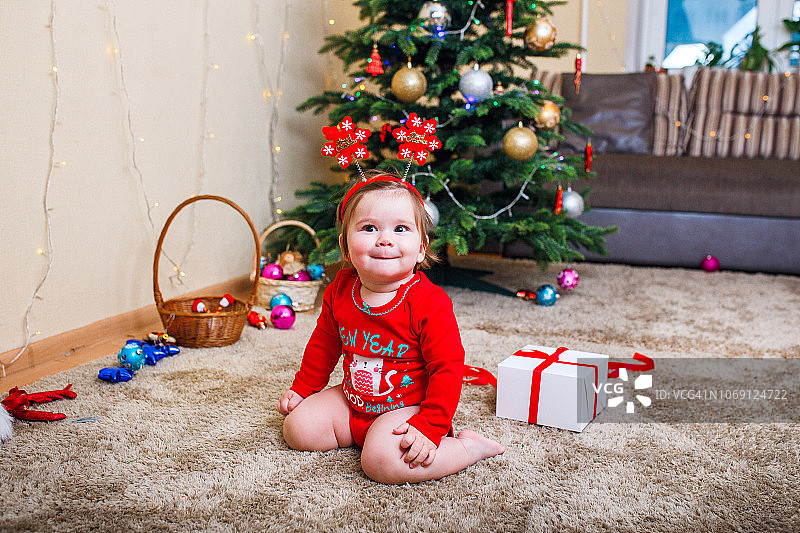 婴儿戴红帽子的圣诞照片。新年假期和圣诞树。图片素材