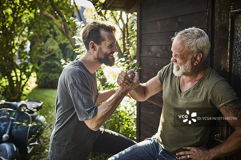 两个快乐的男人握手在花园小屋与旧摩托车在背景图片素材