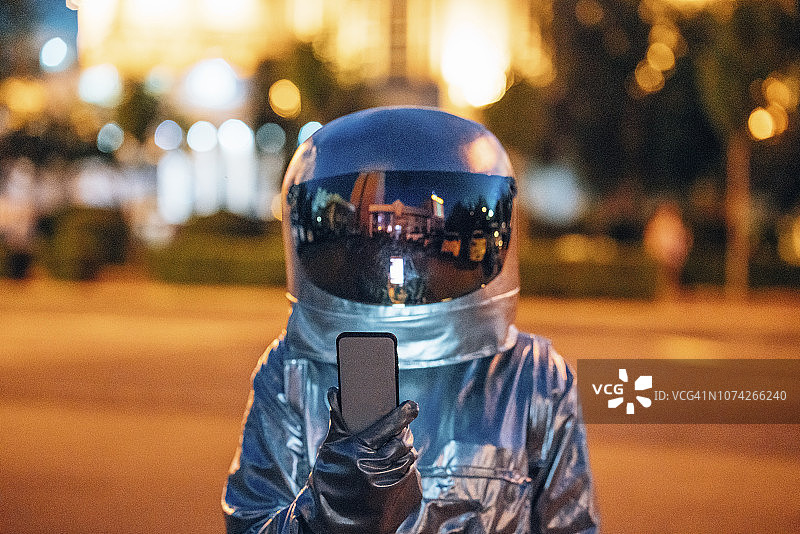宇航员晚上在城市的街道上拿着智能手机图片素材