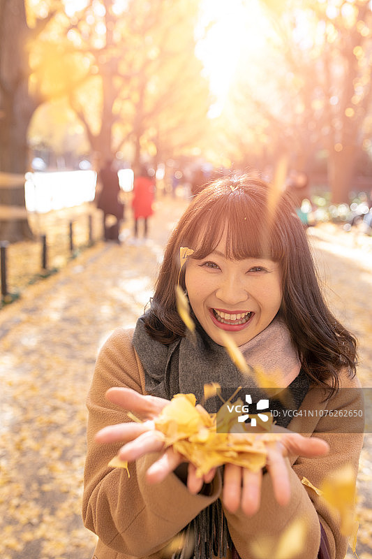 年轻女子在街上捡着落下的银杏叶图片素材