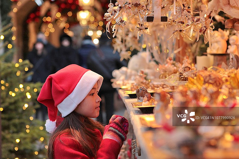 女孩在市场摊位上挑选圣诞装饰品。图片素材