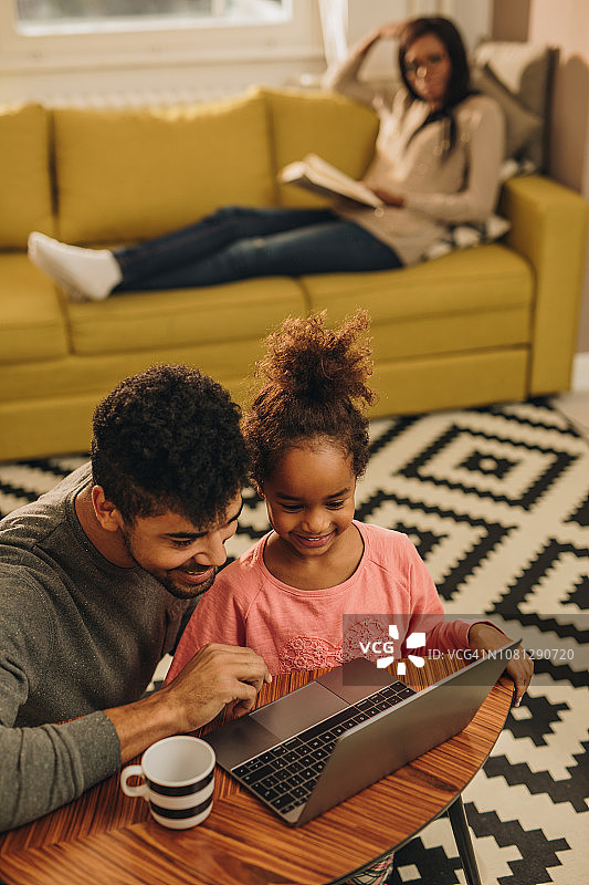 以上的观点，快乐的非裔美国父亲和女儿使用笔记本电脑在家里。图片素材