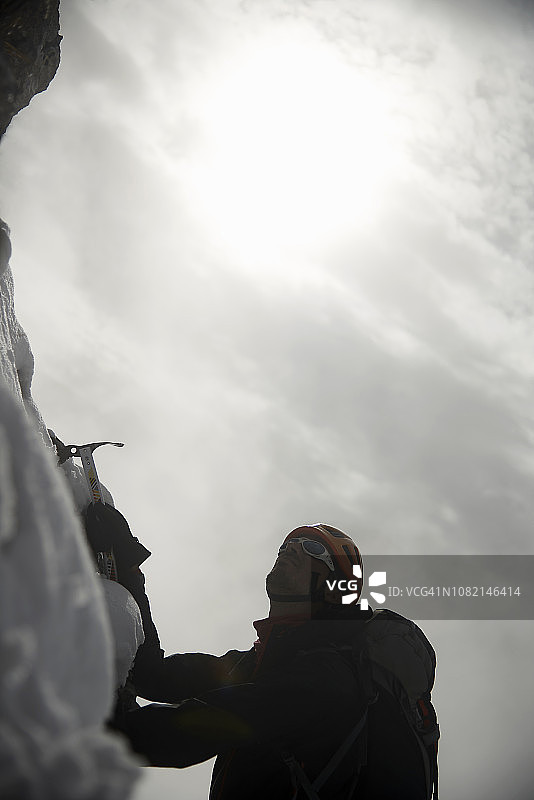 低角度的观点，远足者使用冰斧，而登山对抗天空在冬天图片素材