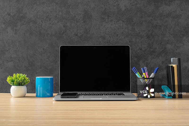 笔记本电脑，办公用品和蓝色咖啡杯在办公桌上。图片素材