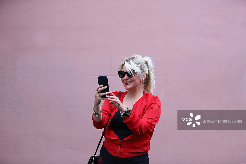 一位年轻女士用手机在粉色背景下自拍图片素材