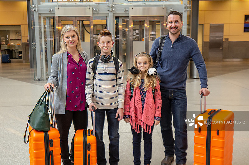 带着行李微笑的家人站在机场停车场的电梯旁。图片素材