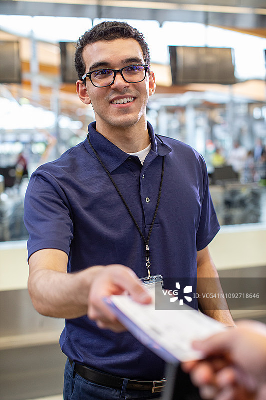 年轻的航空公司值机员微笑着把登机牌递给顾客。图片素材