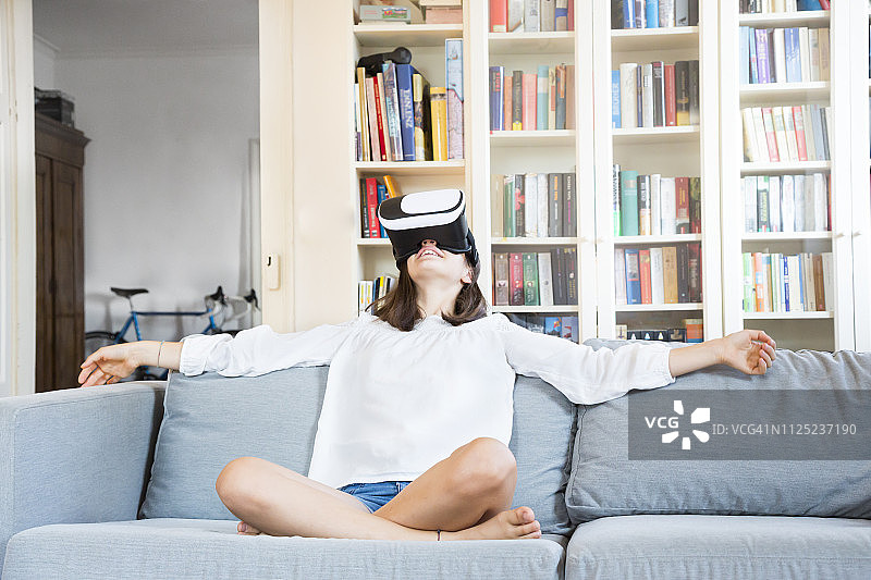 女孩坐在家里的沙发上戴着虚拟现实眼镜图片素材