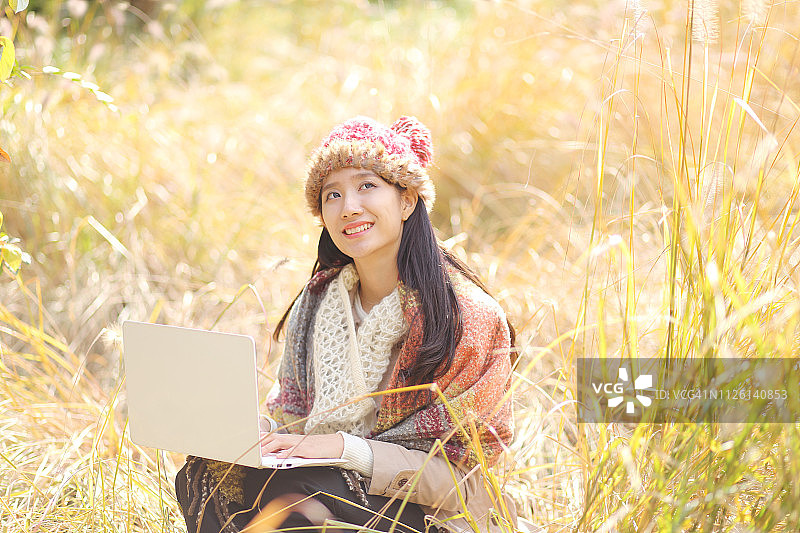 年轻女子在秋季公园使用笔记本电脑图片素材