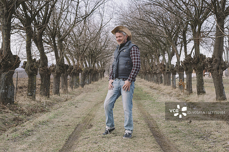 英俊的成年农民戴着牛仔帽站在树巷他的农场入口图片素材