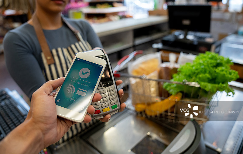 一位面目全非的顾客在超市用智能手机付款图片素材