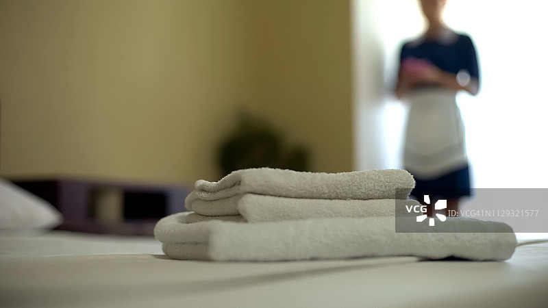 床上放着干净的毛巾，身后是服务员，还有洗衣服务图片素材