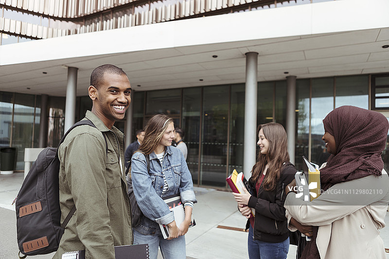 一个微笑的男人站在大学校园里和女性朋友聊天图片素材