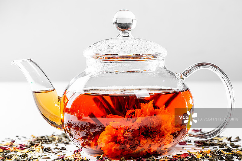 用玻璃茶壶泡茶，还有一朵盛开的大花。白色背景上点缀着异域绿茶的茶壶，还有散落的干茶花瓣和水果图片素材