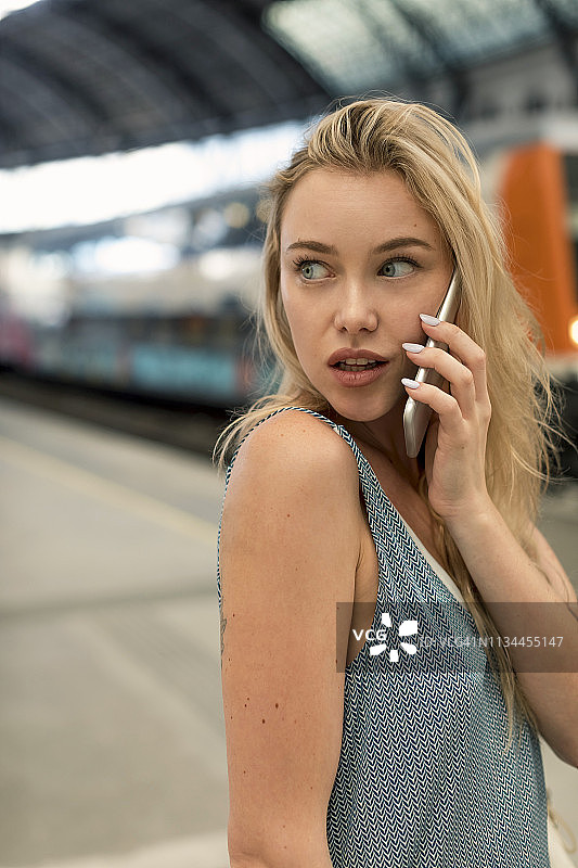 一名年轻女子在火车站用手机四处张望的肖像图片素材
