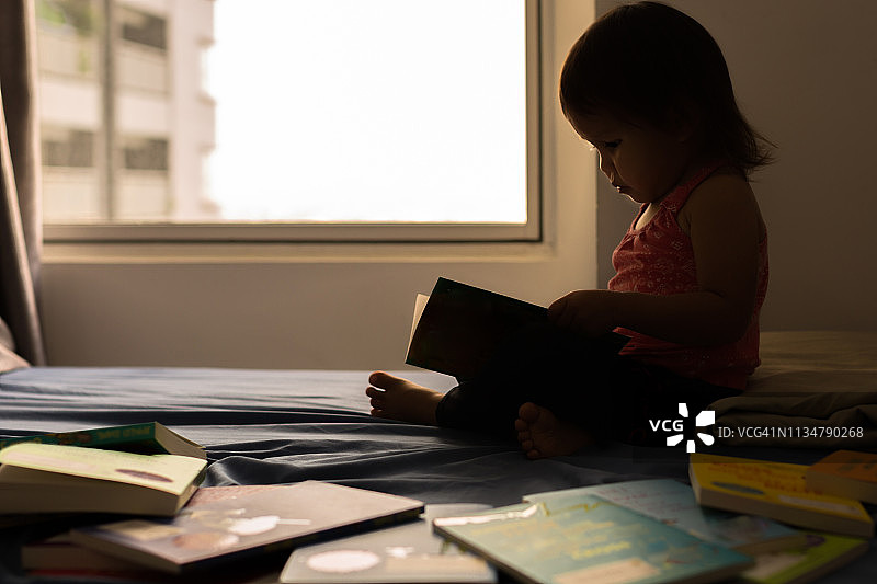 一个小女孩在床上看书。图片素材