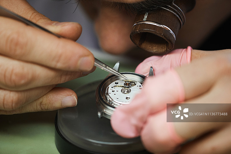 在调整手表齿轮时，用镊子在眼睛上的单眼放大镜中对集中工程师的特写图片素材